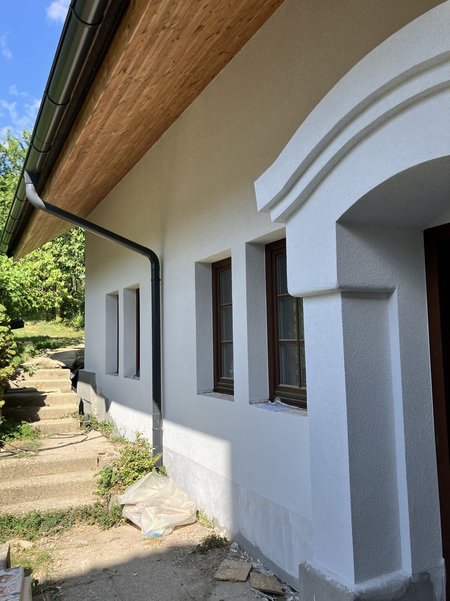 Boční strana bílé přístavby s portálem a kamennými schůdky do zahrady