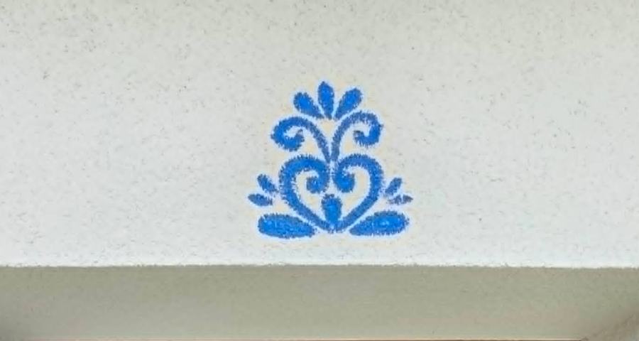 Detail modrého malovaného ornamentu na bílé omítce